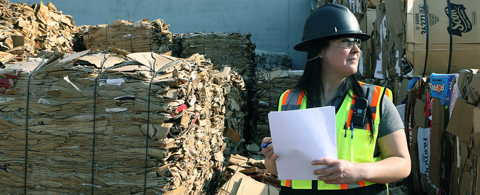 woman looking to the horizon in front of many stacks of bales, while holding a paper